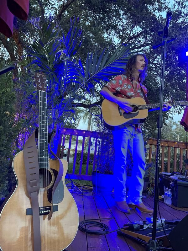 Musician playing acoustic guitar on an outdoor stage lit blue at night